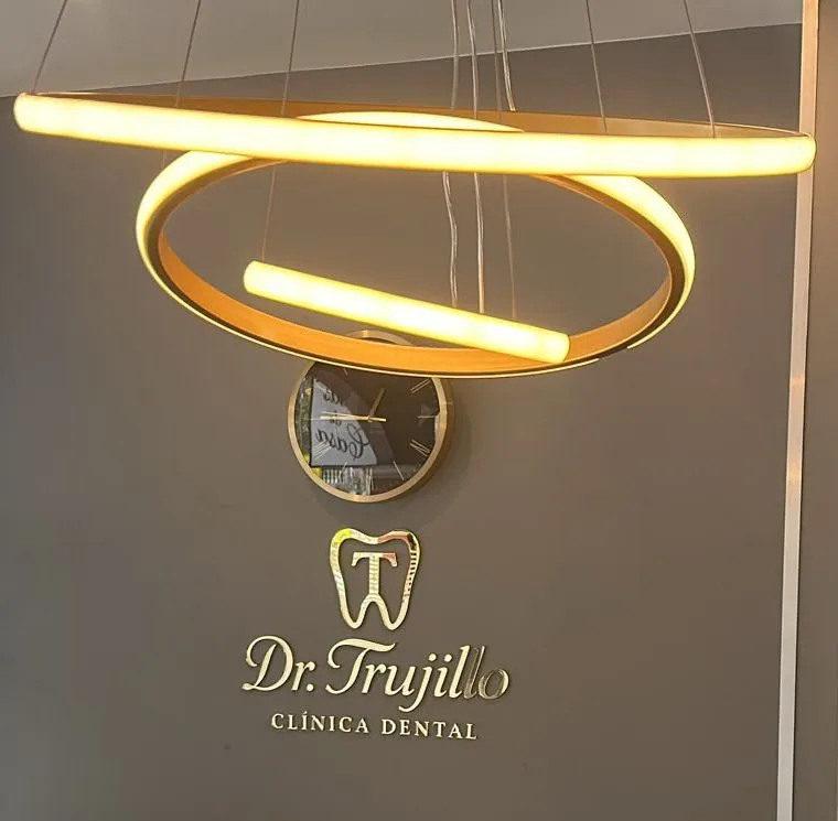 Recepción de la clínica: lámpara de anillos dorados y el logo Dr. Trujillo en relieve sobre la pared